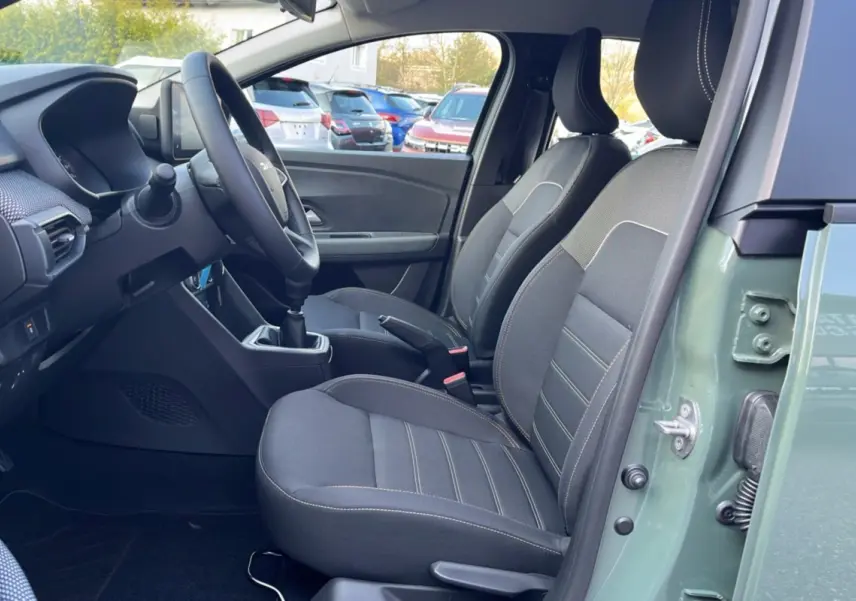 Vue intérieure côté conducteur de la Dacia Sandero Stepway 2025 en kaki lichen, avec sièges tissu gris et boîte manuelle.