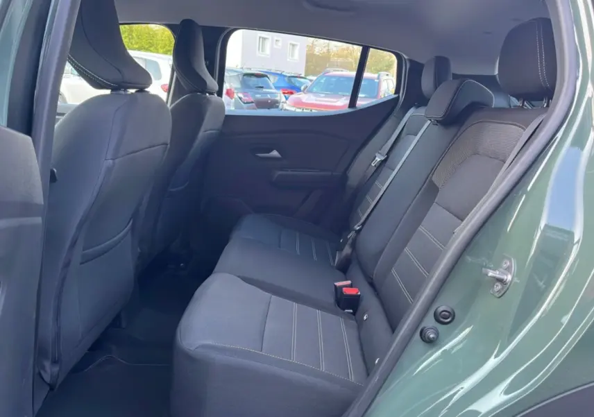 Vue côté droit de l'habitacle arrière d'une Dacia Sandero Stepway 2025 kaki lichen avec sièges en tissu noir et surpiqûres claires.