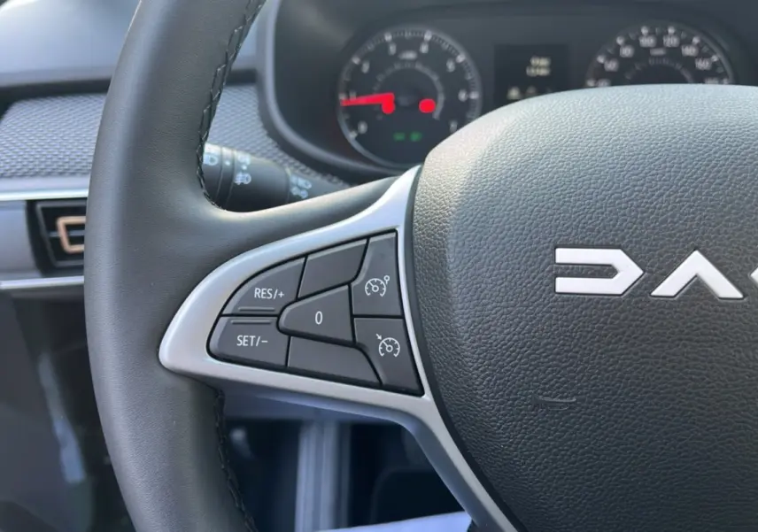 Gros plan sur le volant noir de la Dacia Sandero Stepway 2025 avec commandes de régulateur de vitesse à gauche.