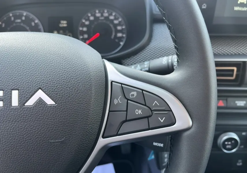 Gros plan sur le volant de la Dacia Sandero Stepway 2025, montrant les commandes multifonctions côté droit en intérieur noir.