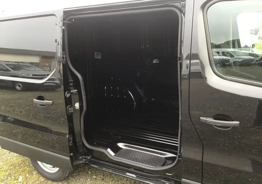 Vue latérale gauche d’un Renault Trafic Fourgon noir 2025 avec porte coulissante ouverte dévoilant l’espace de chargement vide.