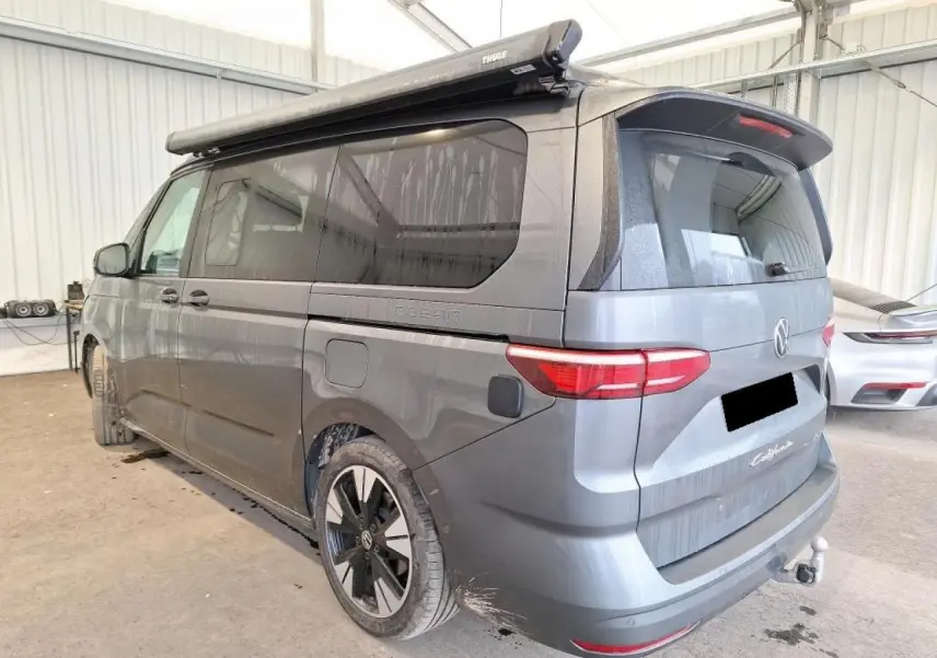 Vue 3/4 arrière droite du Volkswagen California T7 gris Indium avec attelage rabattable et jantes noires brillantes.