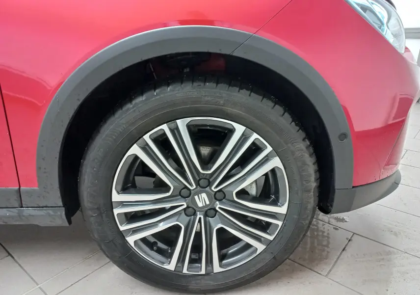 Gros plan sur la roue avant droite d’un SEAT Arona rouge Désir avec jante alliage bicolore et entourage noir.