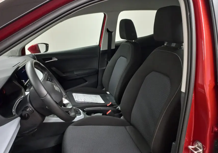 Vue intérieure côté gauche du SEAT Arona rouge Désir, montrant les sièges avant noirs et le volant avec logo SEAT.