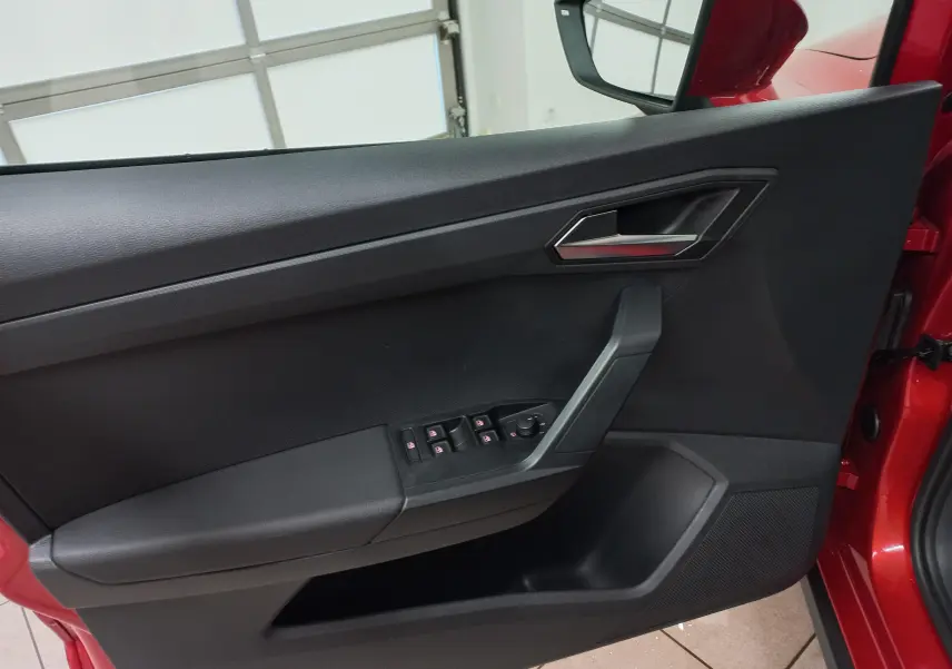 Vue intérieure côté gauche de la porte avant rouge désir avec commandes de vitres et poignée argentée du SEAT Arona 2025.