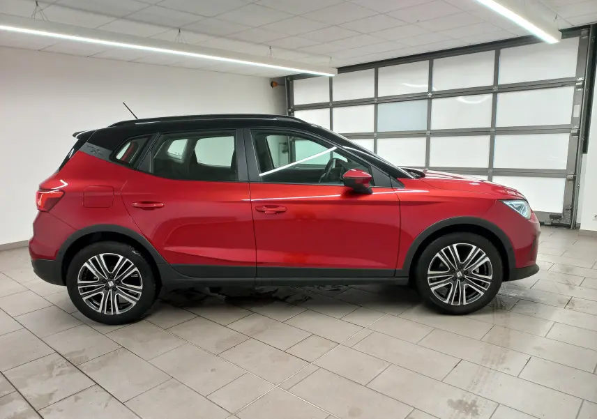 Vue de profil côté gauche du SEAT Arona 2025 rouge Désir avec toit noir Minuit dans un garage intérieur.