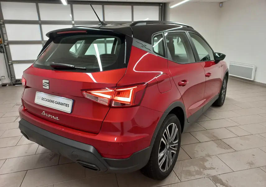 Vue 3/4 arrière droite du SEAT Arona rouge Désir avec toit noir Minuit, en intérieur, mettant en valeur ses feux arrière et jantes.