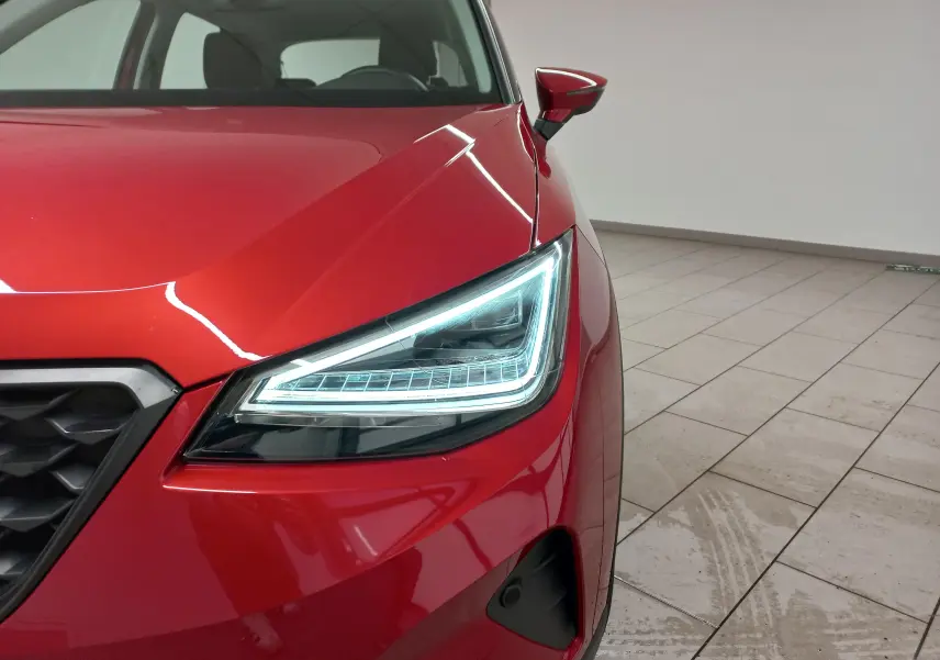 Gros plan sur l’avant droit du SEAT Arona rouge Désir avec phare LED allumé et rétroviseur assorti.