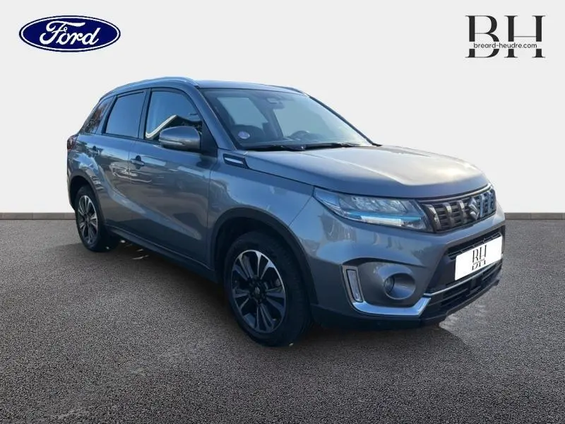 Suzuki Vitara 1.4 Boosterjet Hybrid gris Galactic, vue 3/4 avant avec calandre chromée et jantes alu noires.