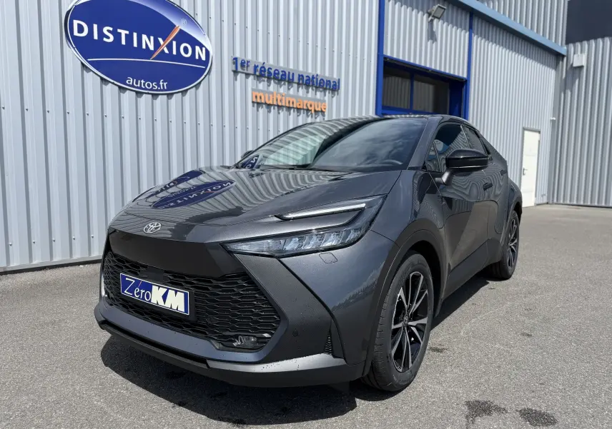 Toyota C-HR 1.8 Hybride gris atlas vu en 3/4 avant droit, avec calandre noire et jantes alliage noires.