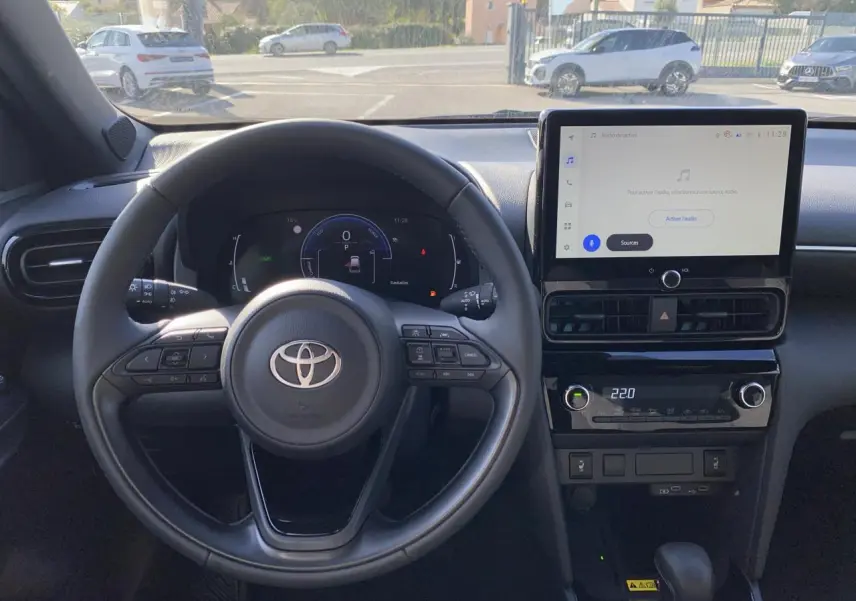 Vue intérieure centrée sur le volant cuir et l'écran tactile du tableau de bord de la Toyota Yaris Cross blanche.