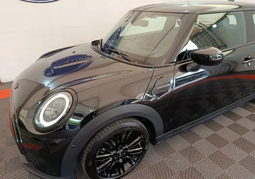 Vue 3/4 avant droit d'une MINI Cooper Edition Premium Plus noire avec jantes noires et phares LED circulaires allumés.