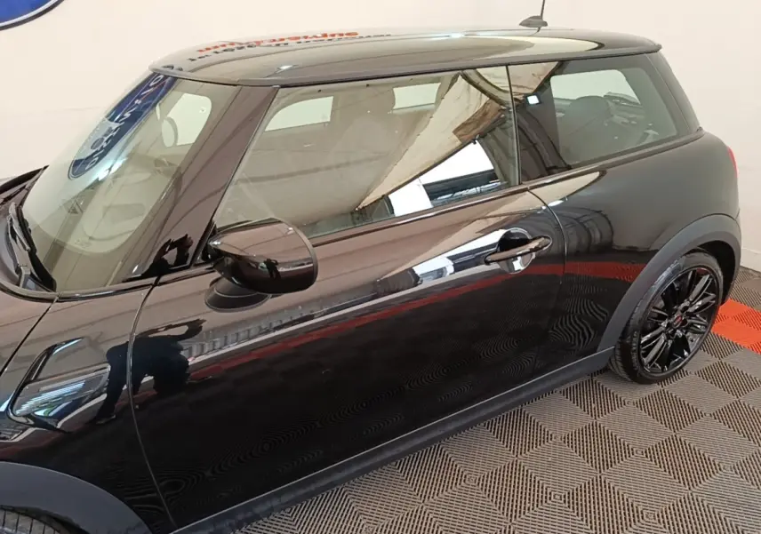 Vue de profil côté gauche d'une MINI Cooper noire avec jantes noires brillantes sur sol à damier.