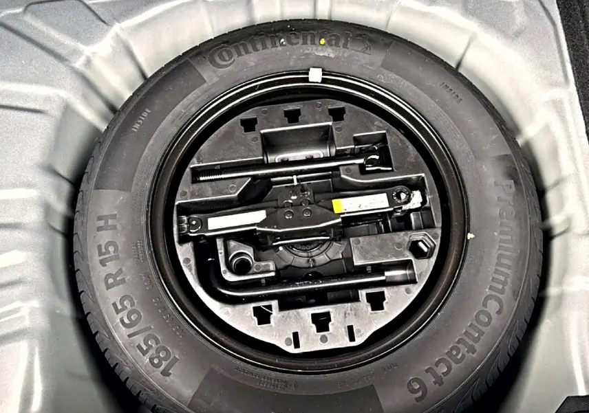 Roue de secours avec kit d'outils intégrés dans le coffre d'une Renault Clio V noire, vue de dessus.