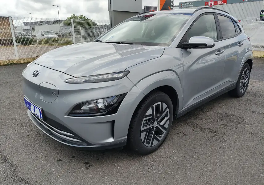 Hyundai Kona Electric gris métallisé vu en 3/4 avant droit, avec jantes alliage et calandre fermée distinctive.