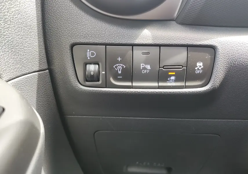 Gros plan sur les commandes de réglage des feux et aides à la conduite dans l'habitacle noir d'une Hyundai Kona Electric 2025.