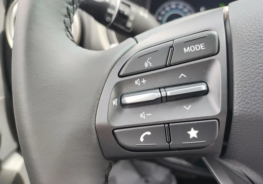 Gros plan sur les commandes audio et vocales au volant cuir du Hyundai Kona Electric gris métallisé 2025.