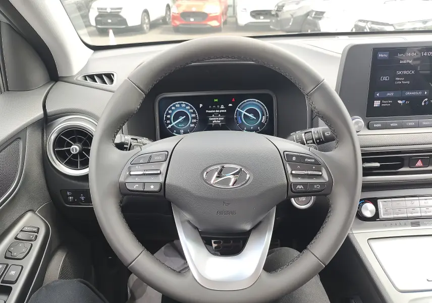 Vue intérieure centrée sur le volant cuir gris du Hyundai Kona Electric 2025 avec tableau de bord numérique et écran tactile.