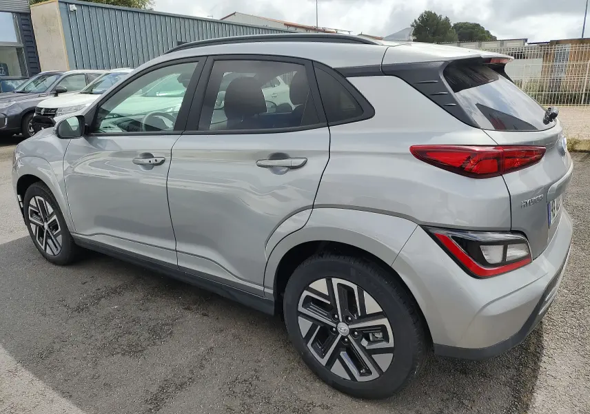 Vue 3/4 arrière côté gauche d'un Hyundai Kona électrique gris métallisé avec jantes alliage et vitres surteintées