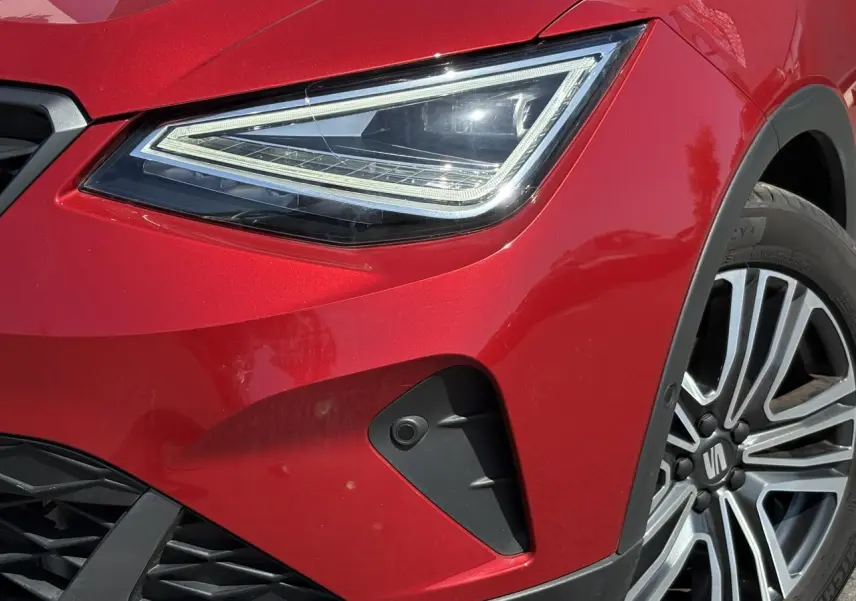 Gros plan sur le phare avant gauche rouge Désir du SEAT ARONA TSI 110 FR avec jante alliage 17 pouces et caméra frontale.