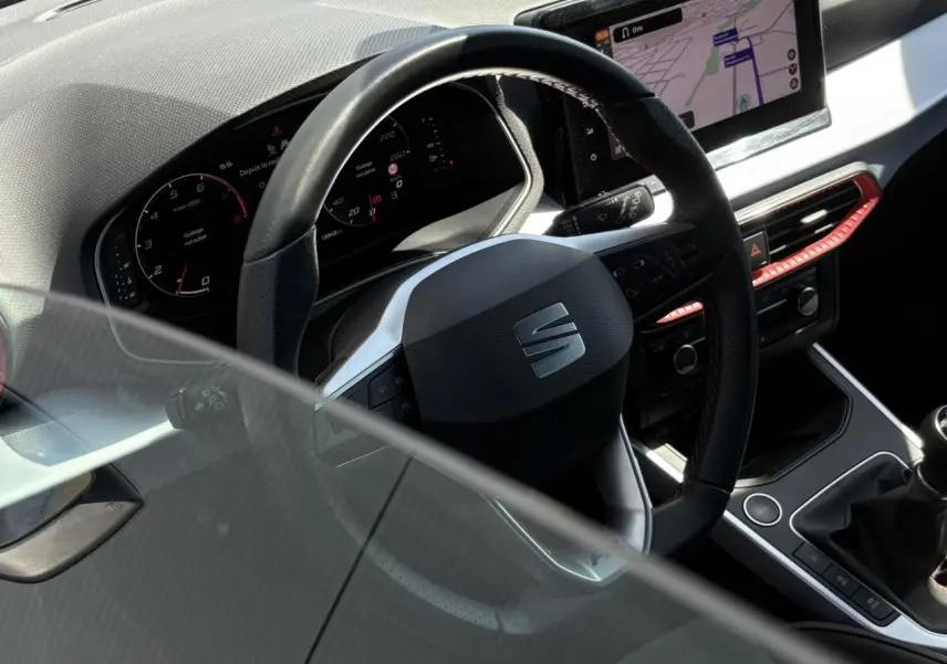 Vue intérieure du volant et tableau de bord numérique d'une SEAT Arona TSI 110 FR avec détails rouges et écran de navigation.