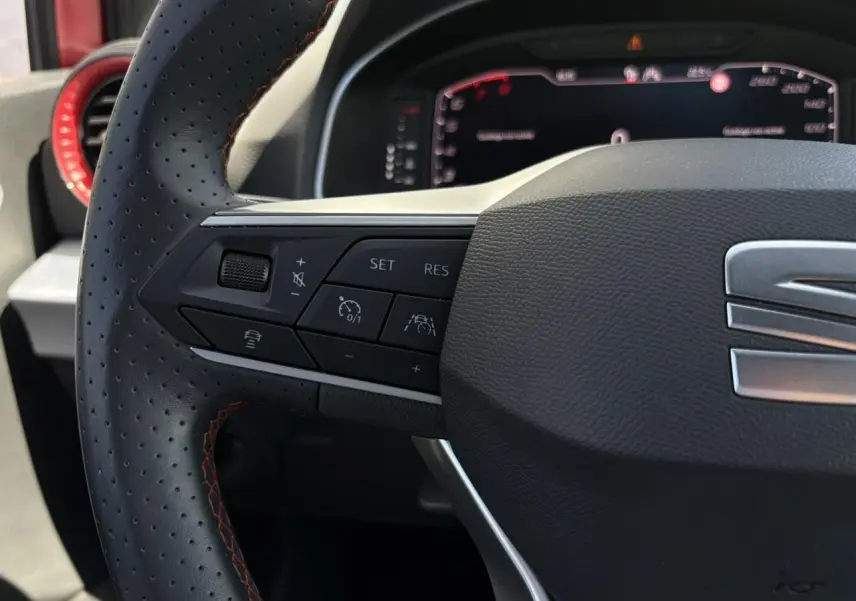 Gros plan sur le volant perforé avec surpiqûres rouges du SEAT Arona TSI 110 FR, boutons de régulateur adaptatif visibles.