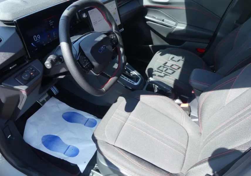 Intérieur avant droit du Ford Puma 2025 avec sièges tissu gris et surpiqûres rouges, volant multifonction et écran digital.