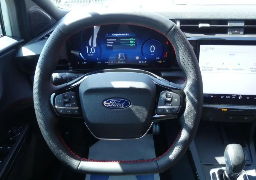 Vue intérieure centrée sur le volant perforé avec surpiqûres rouges et tableau de bord numérique du Ford Puma 2025.