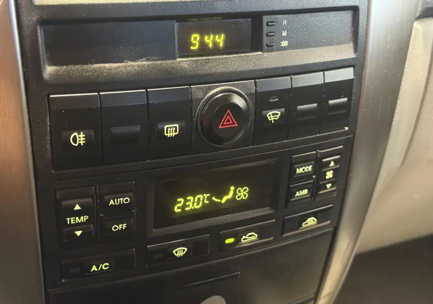 Panneau de commande central noir du Kia Sorento 2005 avec affichage digital de la climatisation réglée à 23°C.