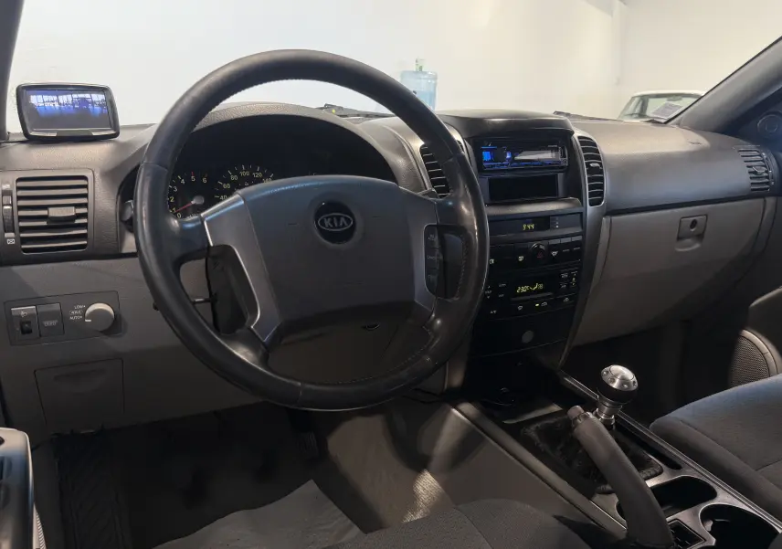 Intérieur du Kia Sorento 2005 gris, vue du poste de conduite avec volant, tableau de bord et levier de vitesses manuel.