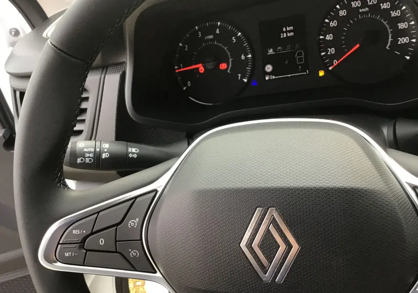 Vue rapprochée du volant et du tableau de bord du Renault Trafic Fourgon blanc, avec commandes au volant et affichage digital.