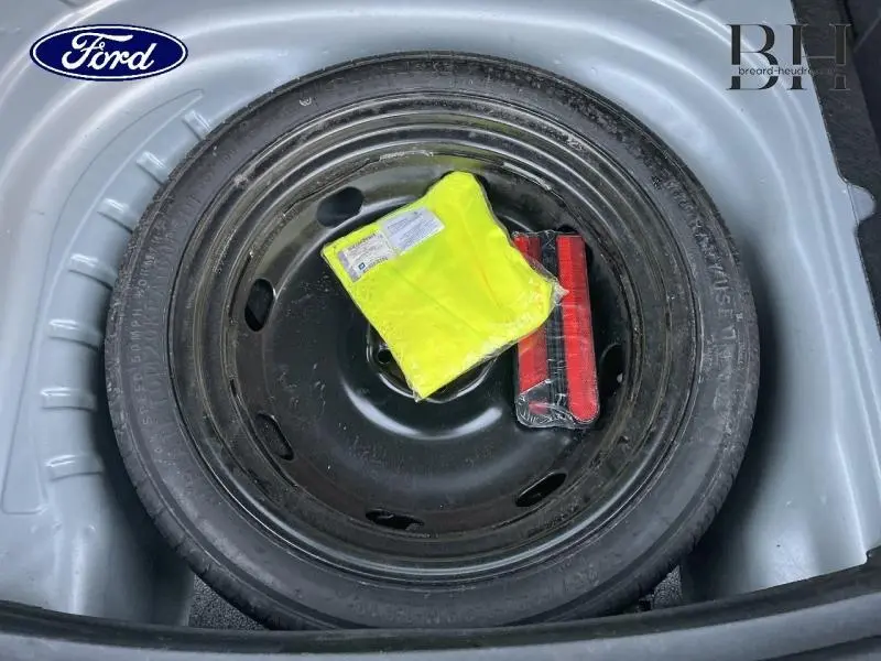 Gros plan sur la roue de secours noire dans le coffre d'une SEAT LEON ST 1.0 eTSI 110ch Urban gris urbain métal, avec gilet jaune et triangle de signalisation.