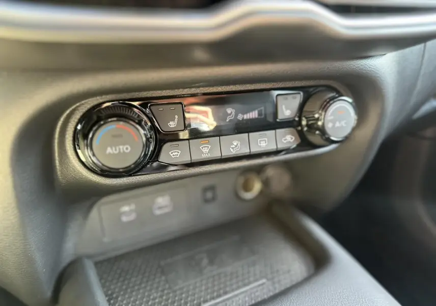 Gros plan sur la console centrale du Nissan Juke 2025 noire, montrant les commandes de climatisation automatique et sièges chauffants.