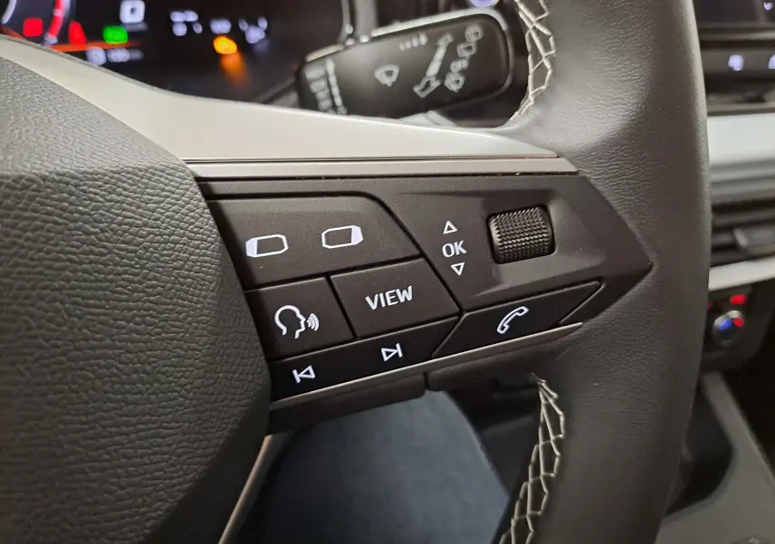 Gros plan sur les commandes multifonctions côté gauche du volant noir de la SEAT Ibiza 2025, avec boutons rétroéclairés blancs.