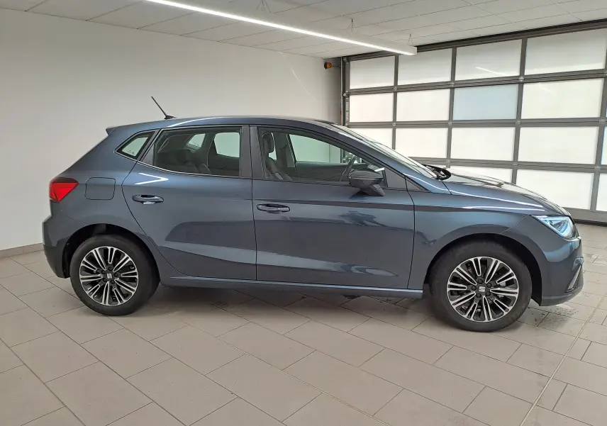Vue latérale droite d'une SEAT Ibiza 2025 gris magnétique avec jantes alliage et feux avant allumés en intérieur.