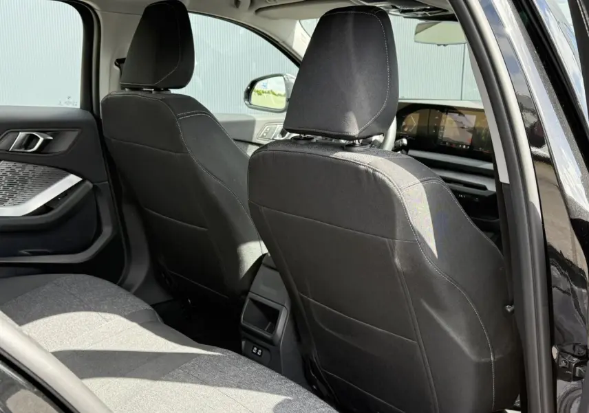 Vue intérieure arrière côté gauche de la BMW Série 1 118dA 2025 en Saphirschwarz avec sellerie tissu anthracite.