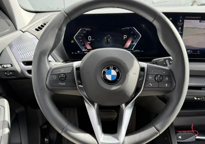 Vue rapprochée du volant noir multifonctions de la BMW Série 1 118dA 2025 avec tableau de bord numérique allumé.
