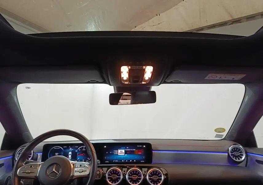 Vue intérieure avant du tableau de bord et volant cuir de la Mercedes CLA 200 d AMG Line 2022 avec éclairage d'ambiance bleu.