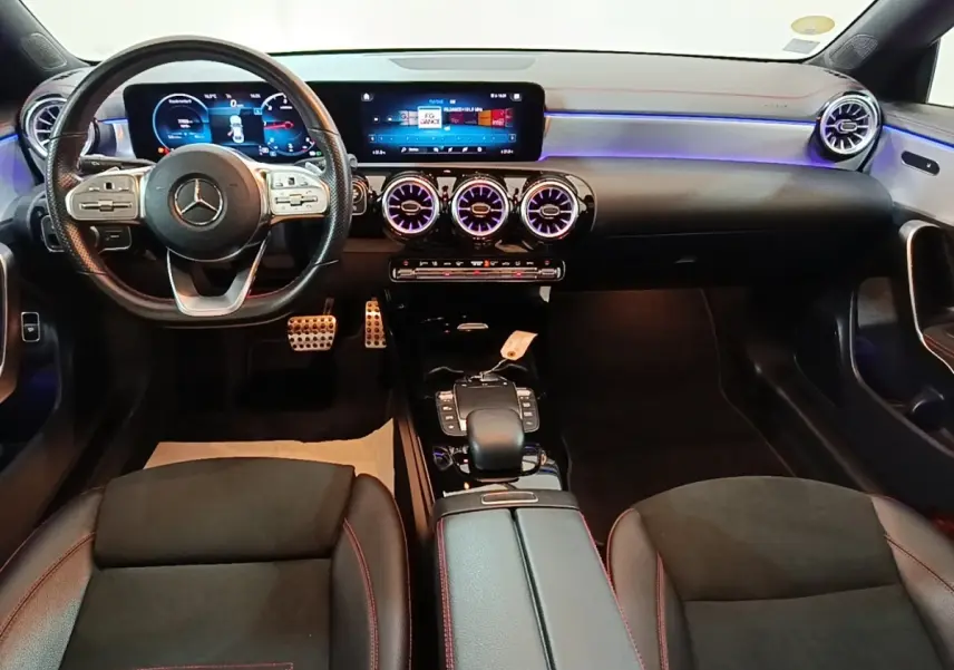 Vue intérieure avant du Mercedes CLA 200 d AMG Line 2022, tableau de bord noir avec éclairage LED violet et volant cuir.