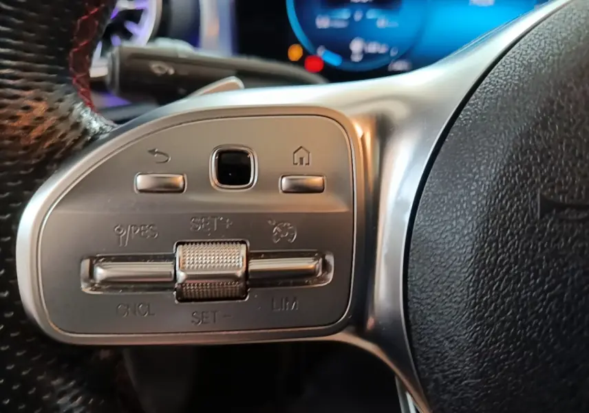 Gros plan sur les commandes du volant en cuir noir d’une Mercedes CLA 200 d AMG Line 2022, avec affichage digital bleu en arrière-plan.
