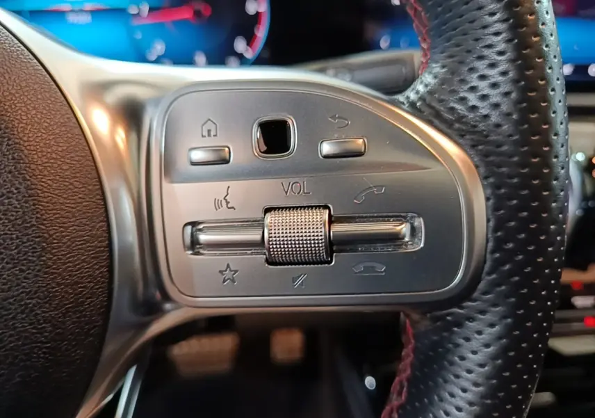 Gros plan sur les commandes argentées du volant cuir perforé noir d’une Mercedes CLA 200 d AMG Line 2022.