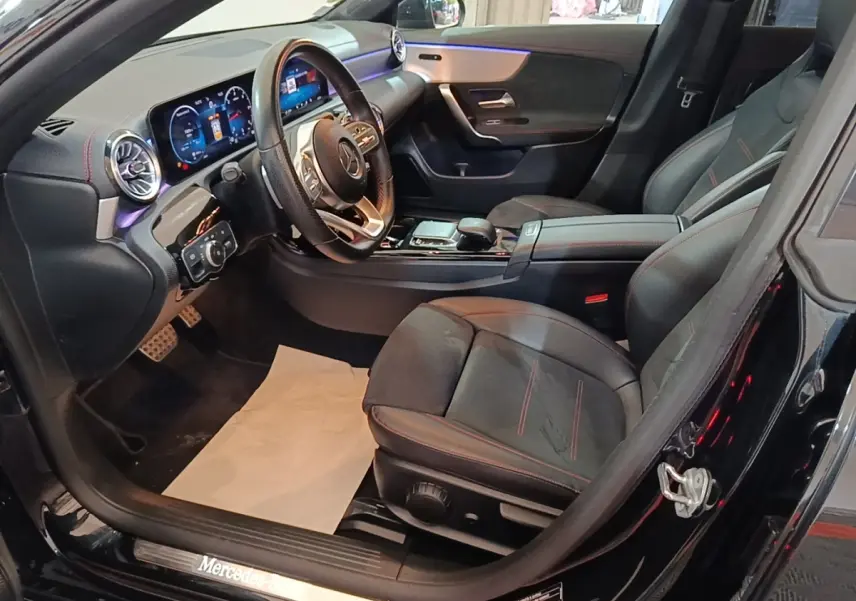 Vue intérieure côté conducteur de la Mercedes CLA 200 d AMG Line noire, avec tableau de bord digital et sièges sport noirs.