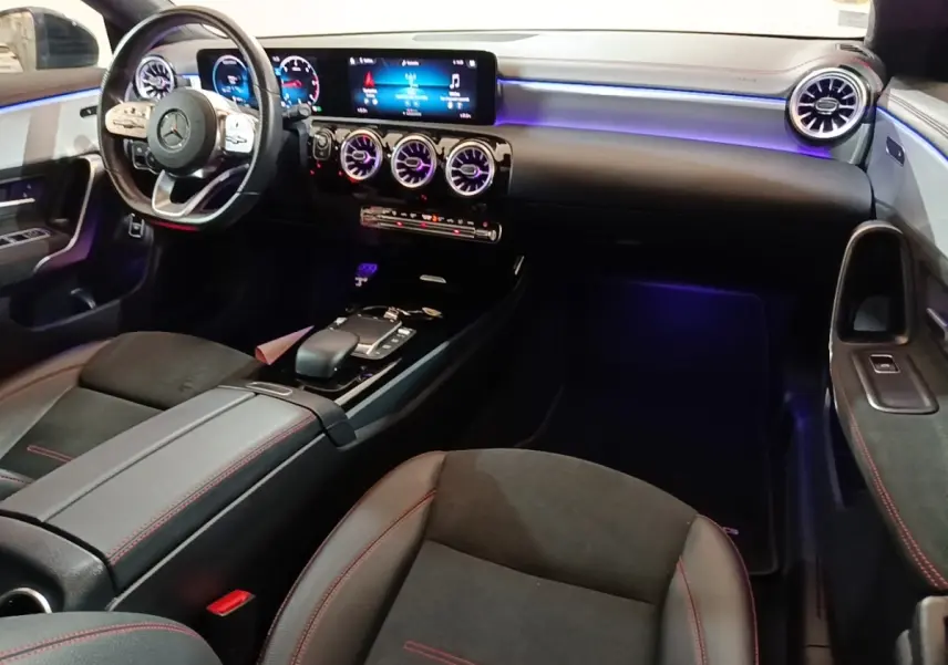 Vue intérieure côté conducteur de la Mercedes CLA 200 d AMG Line 2022, avec éclairage d'ambiance violet et tableau de bord numérique.