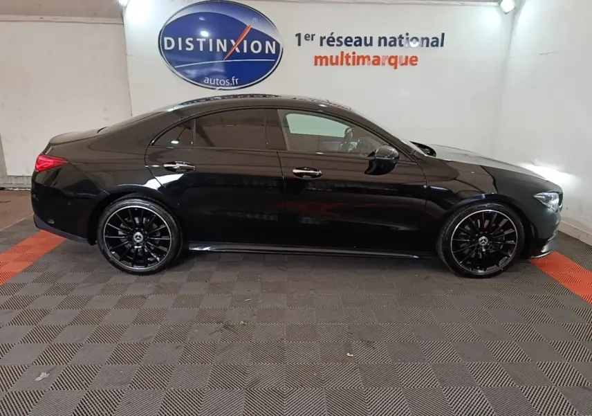 Vue de profil côté gauche d'une Mercedes CLA 200 d AMG Line noire, avec jantes noires et vitres teintées, en intérieur showroom.