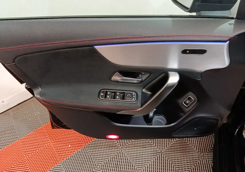 Détail de la porte côté gauche de la Mercedes CLA 200 d AMG Line noire, avec garniture noire, surpiqûres rouges et insert aluminium.