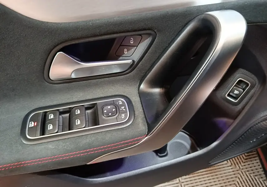 Gros plan sur la porte côté gauche d'une Mercedes CLA 200 d AMG Line noire, avec commandes de vitres et poignée alu.