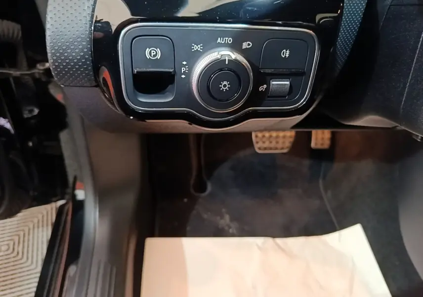 Gros plan sur les commandes d’éclairage et frein à main électrique dans l’habitacle noir d’une Mercedes CLA 200 d AMG Line 2022.
