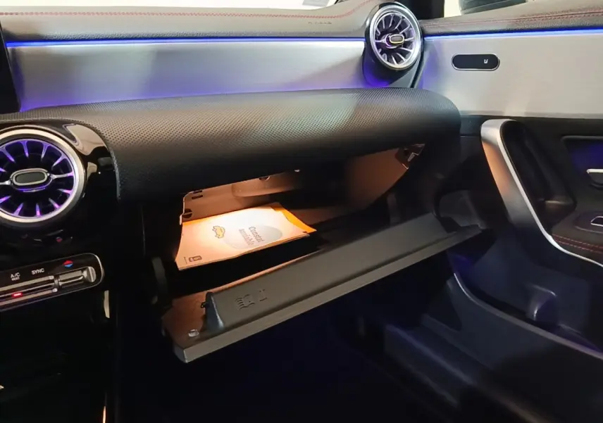 Vue intérieure côté passager de la Mercedes CLA 200 d AMG Line 2022, boîte à gants ouverte avec éclairage d'ambiance violet.