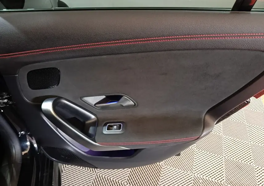 Gros plan sur la porte intérieure côté gauche noire avec surpiqûres rouges et poignée alu de la Mercedes CLA 200 d AMG Line.