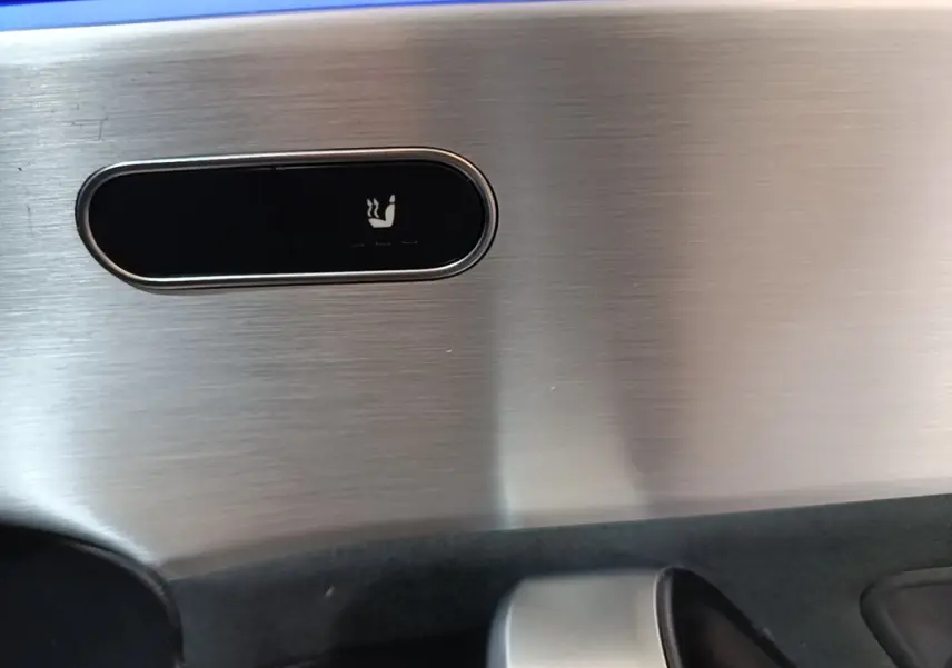 Gros plan sur le bouton de siège chauffant sur la garniture intérieure en aluminium brossé d’une Mercedes CLA 200 d AMG Line noire.